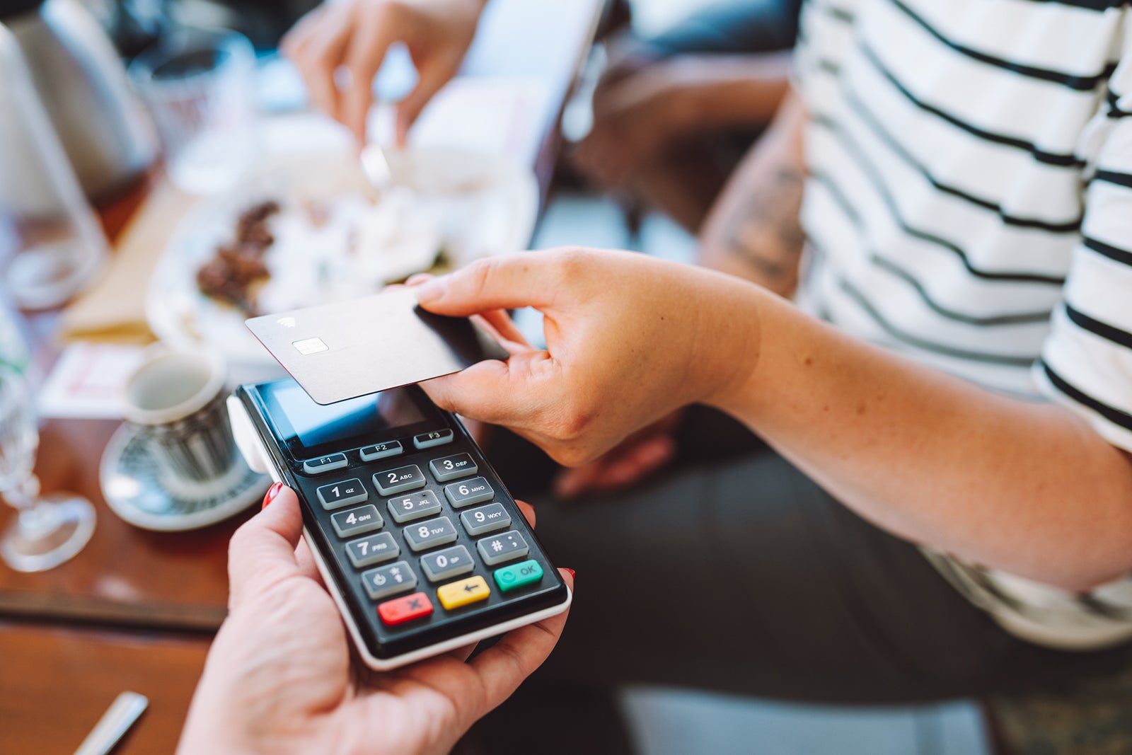 Tap to pay, cashless. Cropped woman hand holding credit card to pay in cafe for food and drinks. Focus on hand and card reader. Close up
